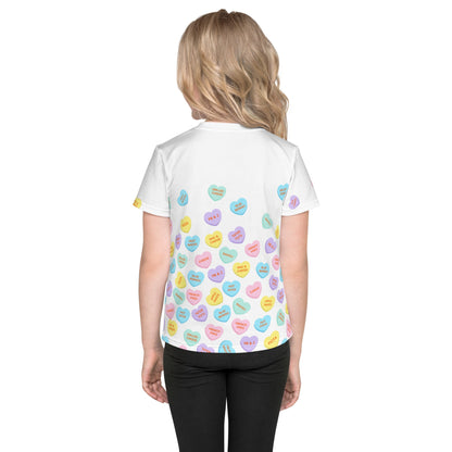 Chunky Deli product image: Close-up of a girl wearing the "Candy Hearts" t-shirt (white with colorful candy hearts featuring food illustrations) from the back, showing the design on the back of the shirt. She is wearing black pants and standing against a 